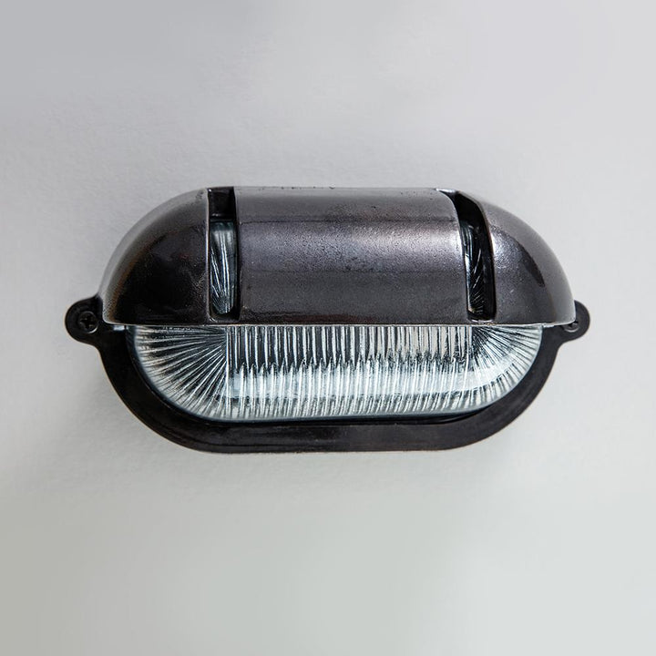 An Old School Electric Oval Bulkhead With Eyelid Wall Light illuminating a white wall.