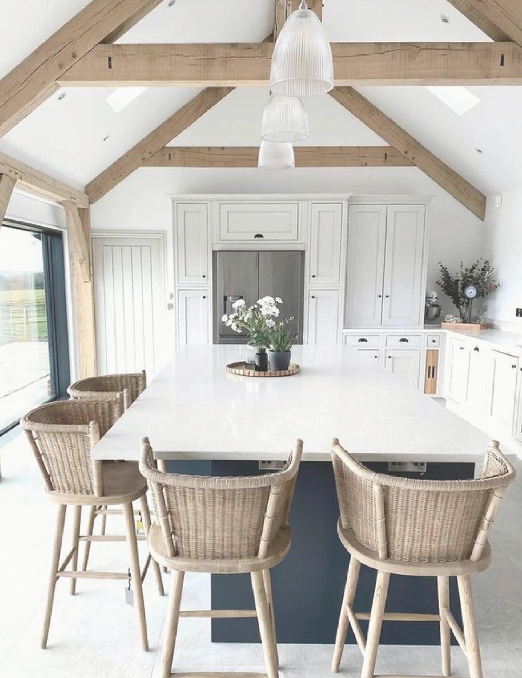 A white kitchen with wooden beams and stools.