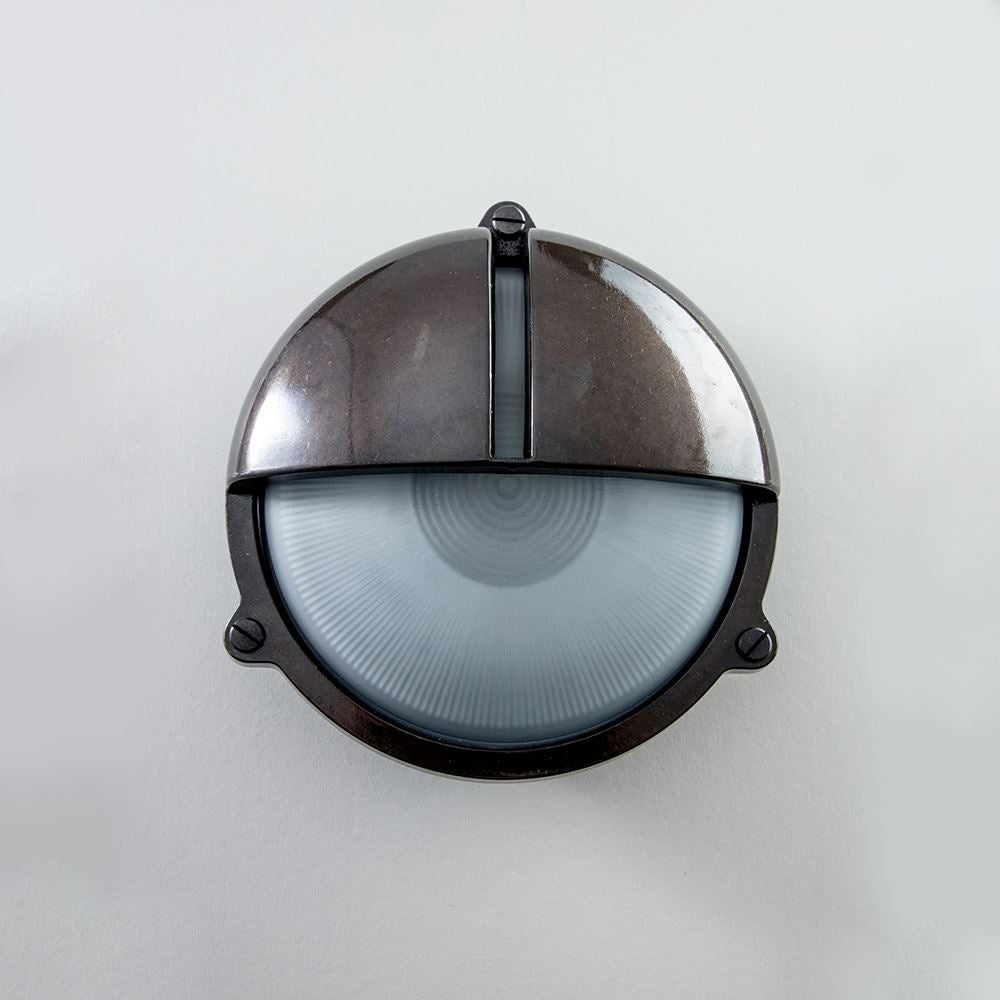 An Old School Electric Round Bulkhead With Eyelid Wall Light on a white outdoor wall.