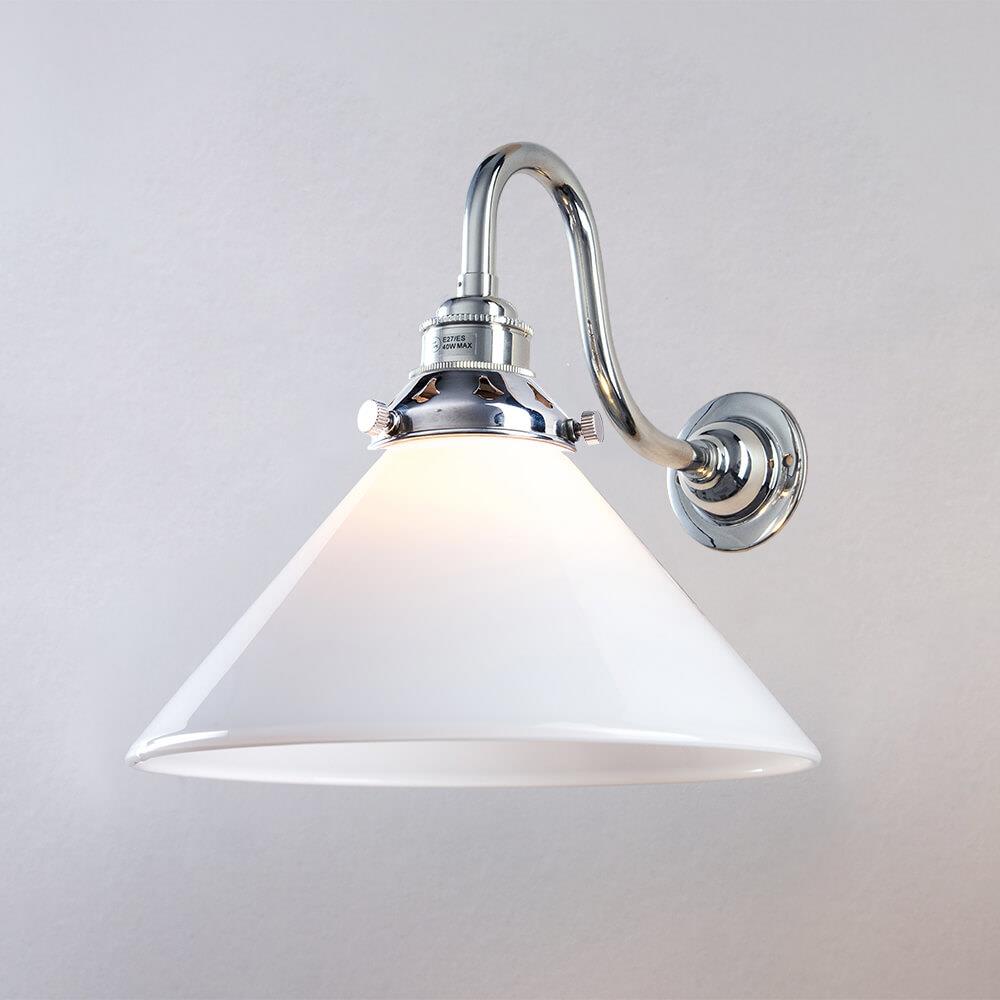 An Old School Electric Conical Glass Wall Light with a white shade on a white wall. The lighting fixture emits a soft glow, illuminating the surrounding space.
