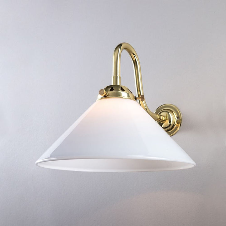A Conical Glass Wall Light (B22) with a white shade. This Old School Electric lighting fixture combines the elegance of a brass frame with the soft glow emitted by an electric light. The white shade adds a touch of sophistication to.