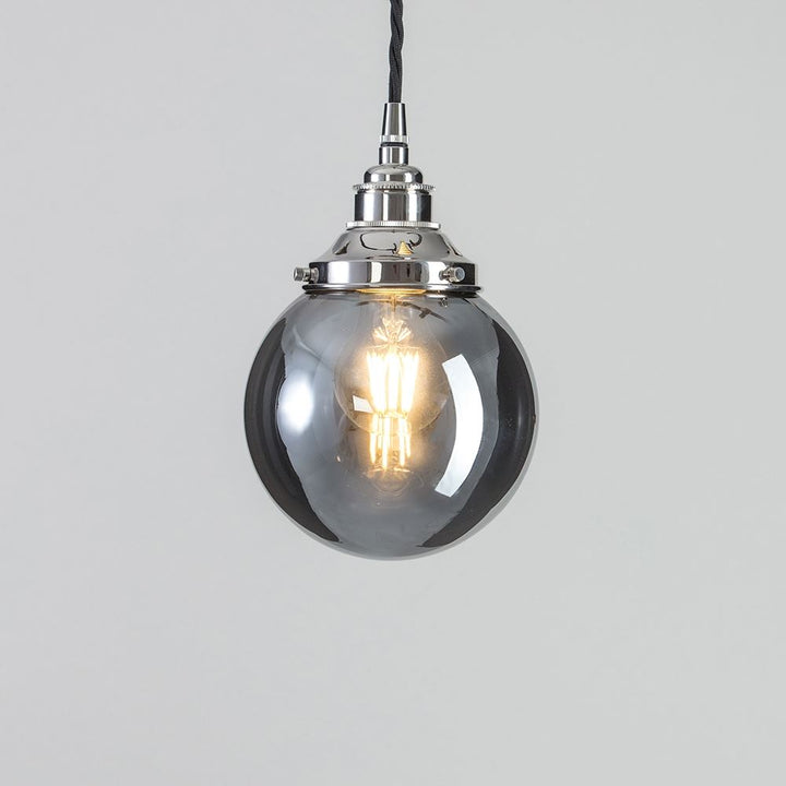 A Globe Blown Smoked Glass Pendant Light with a clear glass globe, perfect for adding an elegant touch to any space. This Old School Electric lighting fixture features a sleek design that seamlessly combines style and functionality. Illuminate your home with the Globe Blown Smoked Glass Pendant Light from Old School Electric.