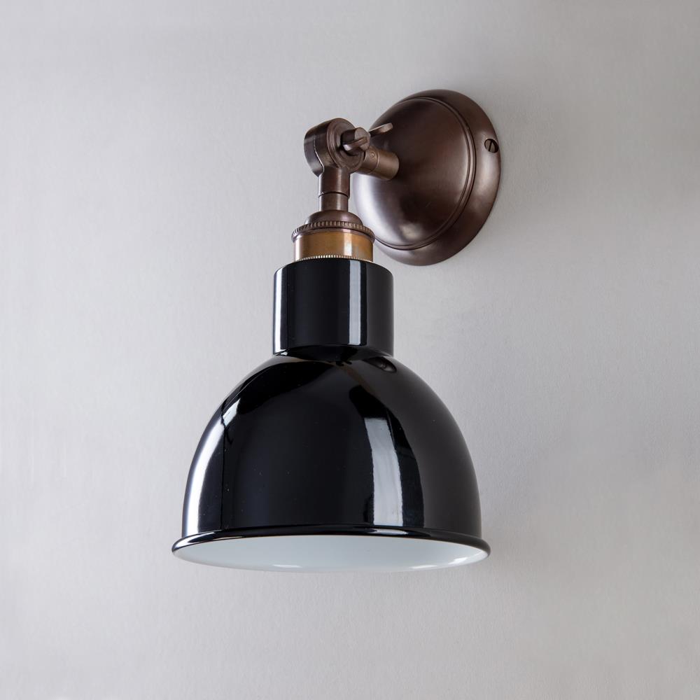 A black and brass Churchill Short Arm Wall Light by Old School Electric illuminating a white wall.