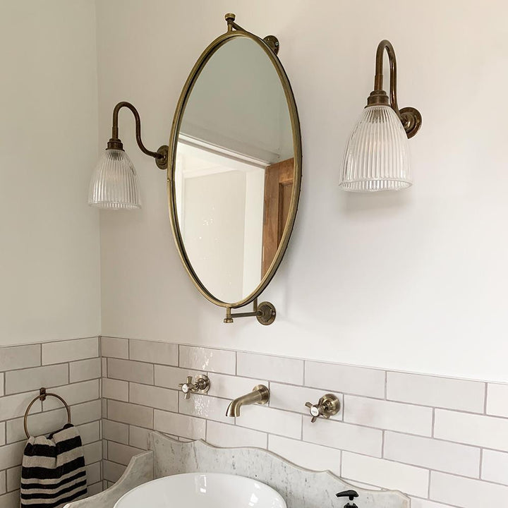 A bathroom with a white sink and a mirror above it, featuring the Old School Electric Elongated Swan Arm Prismatic Bathroom Wall Light.