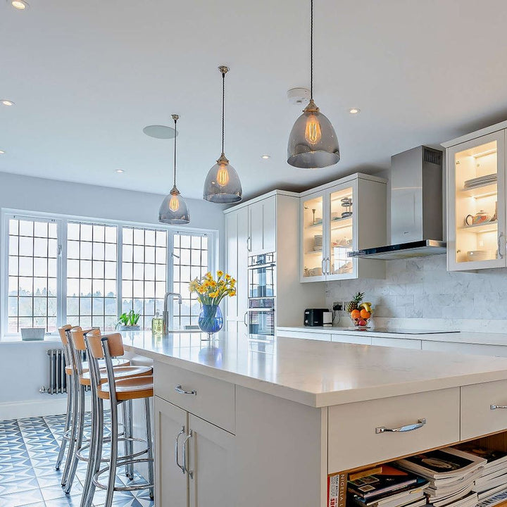 A kitchen with a large island featuring beautiful Old School Electric Bell Blown Smoked Glass Pendant Lights hanging above, creating an enchanting ambiance. The island is complemented by chic stools, providing stylish and comfortable seating.