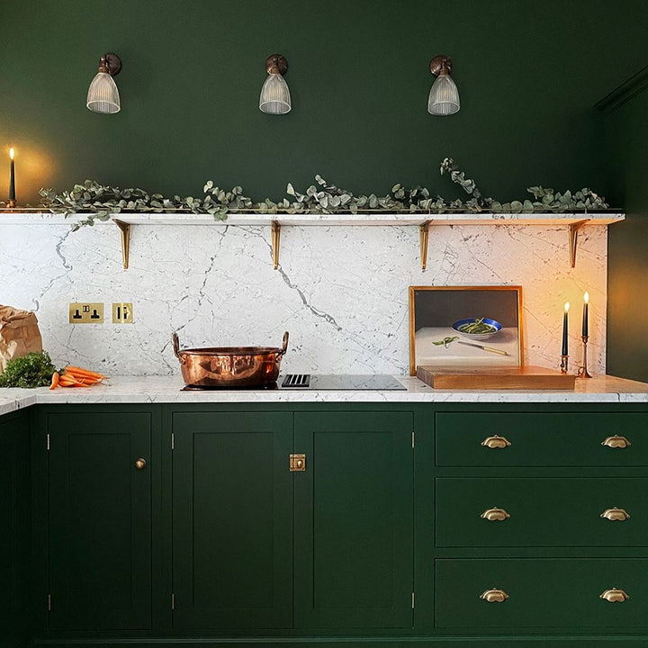 A kitchen with green cabinets and gold accents featuring Old School Electric's Elongated Prismatic Adjustable Arm Wall Light.